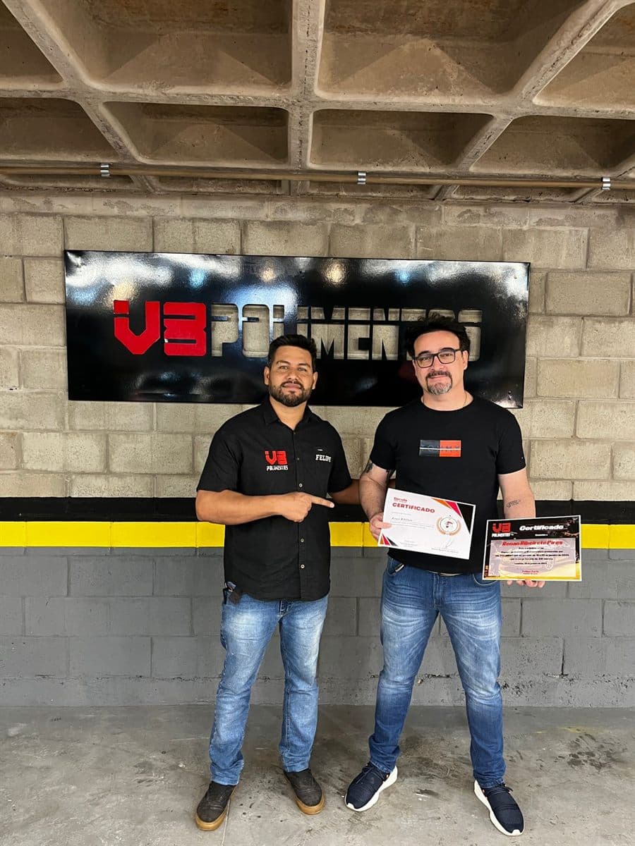 Aluno com certificado em frente ao painel da V8