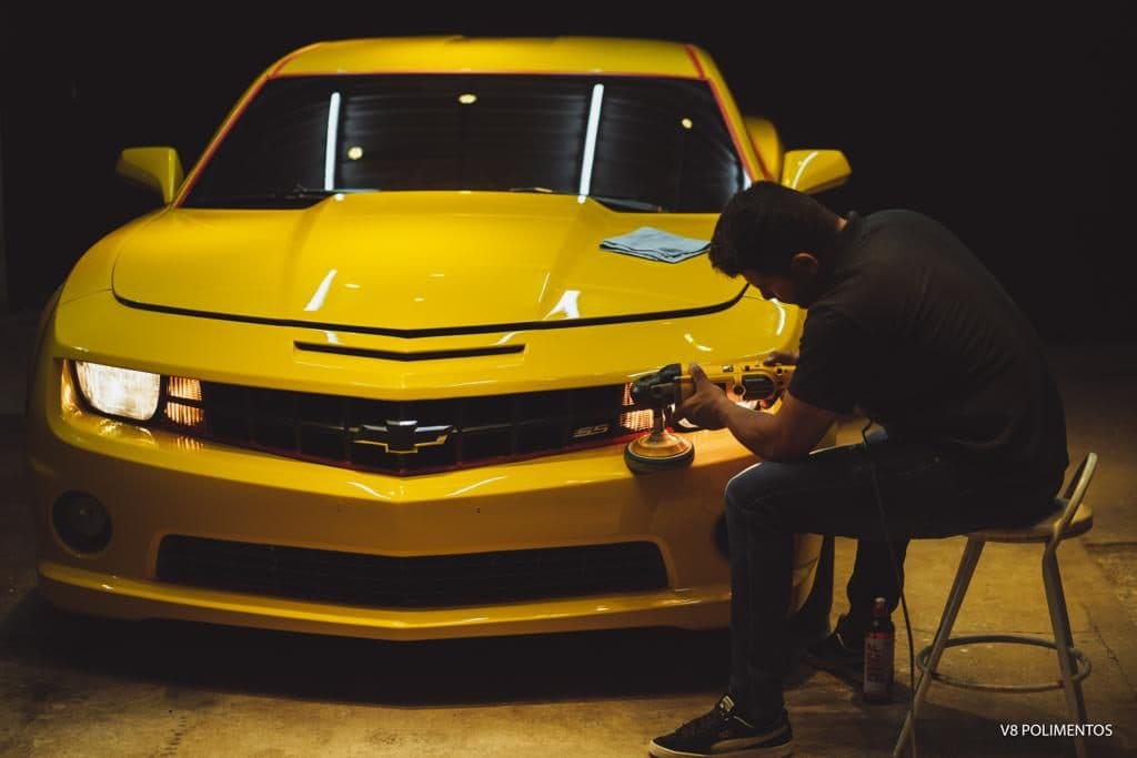 Felipe trabalhando o farol de um Camaro amarelo no box da V8 Polimentos